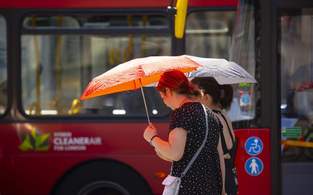 Kobiety używają parasoli, aby chronić się przed słońcem podczas fali upałów w Londynie.