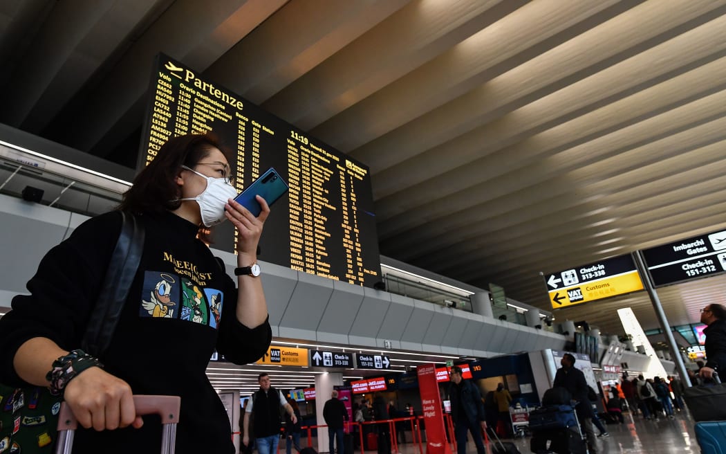 Pasażerka w masce oddechowej rozmawia na swoim smartfonie przy tablicy odlotów na rzymskim lotnisku Fiumicino.