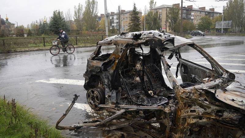 Mężczyzna jedzie na rowerze przed samochodem uszkodzonym w rosyjskim bombardowaniu w centrum Bachmutu.